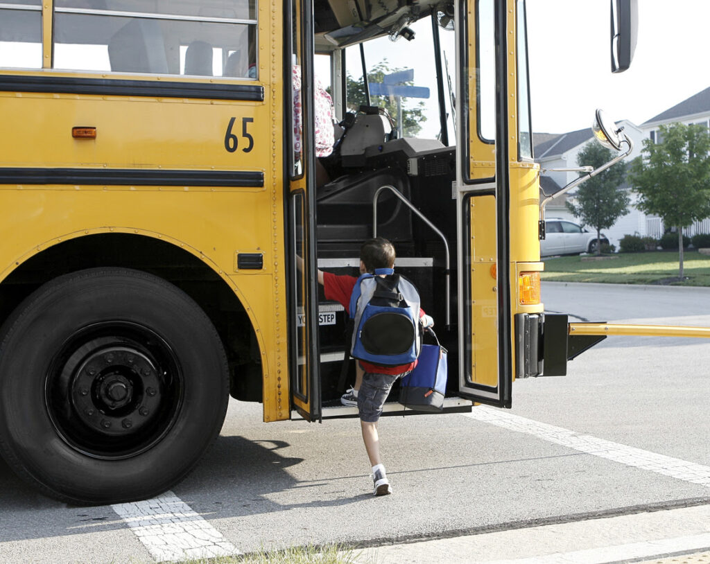 A young boy entering a yellow bus to head to school.
