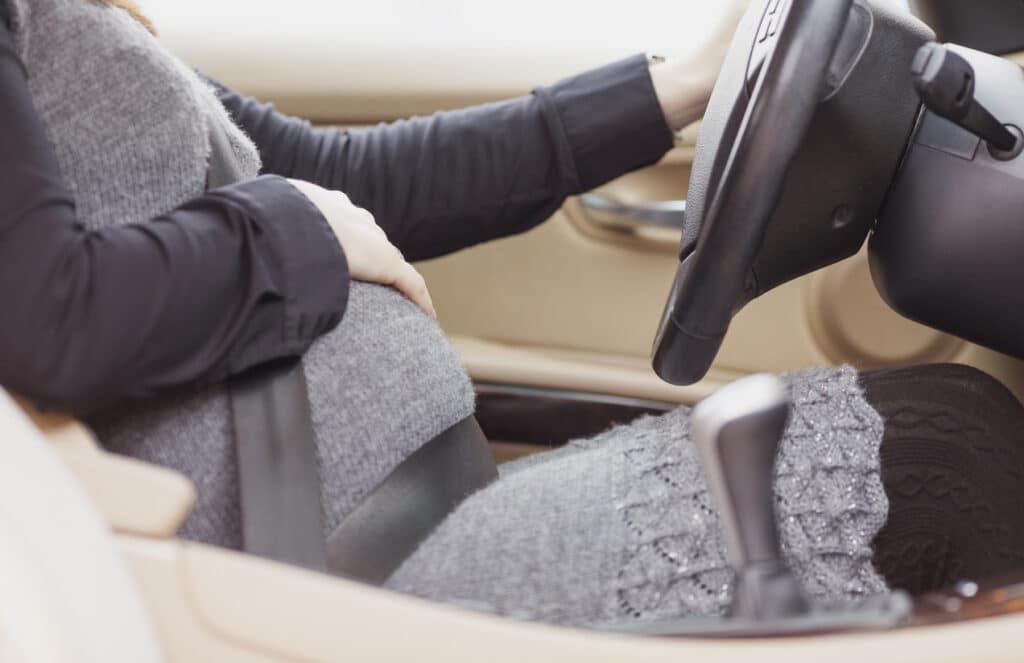 Pregnant woman driving a car with one hand.