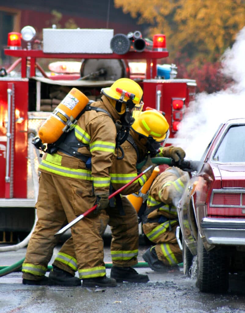 Firefighters in uniforms working to extinguish a car fire.
