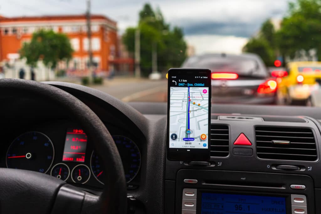Driving and using Waze maps application on smartphone on car dashboard.
