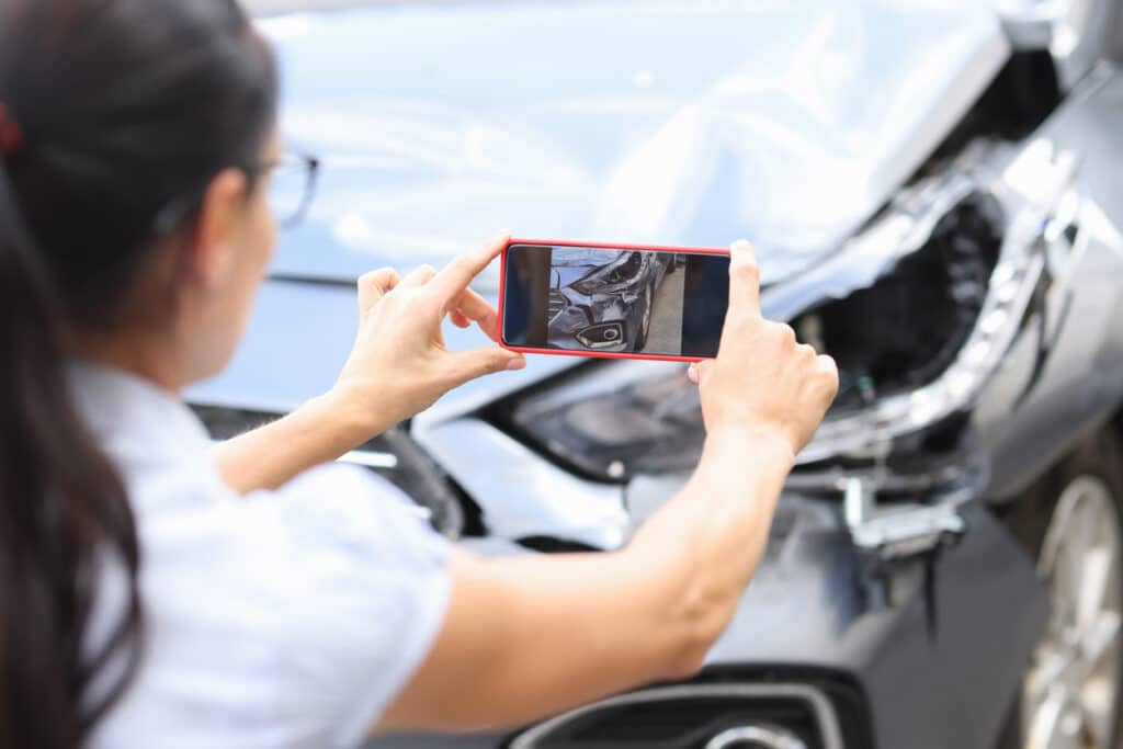 A woman taking a picture of her damaged car.