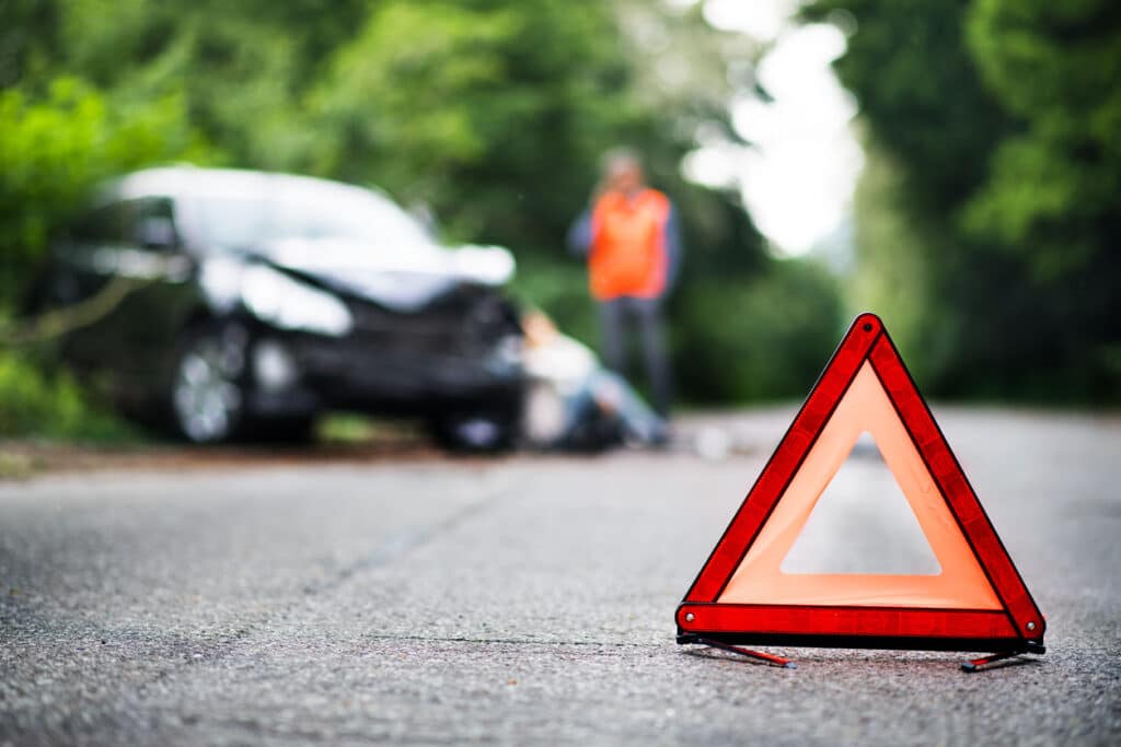 A red emergency triangle on a road in front of a car accident scene.