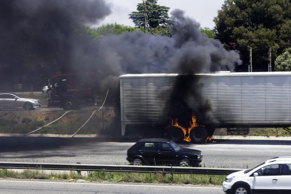 Truck wheels on fire on the highway with firefighters about to extinguish the fire.