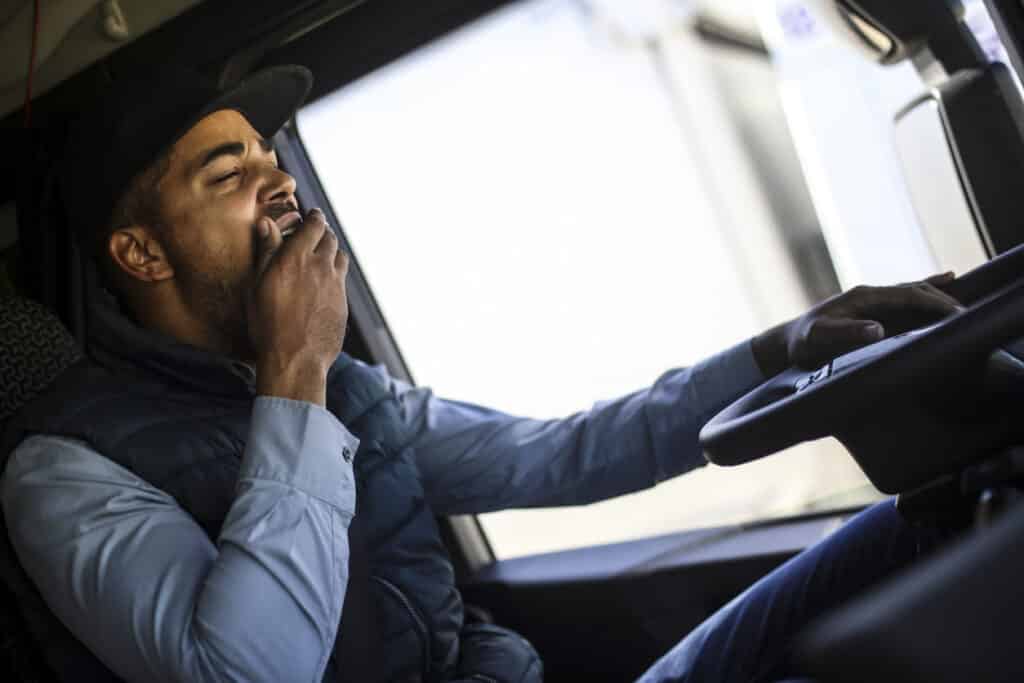 A truck driver yawning while driving on the highway.