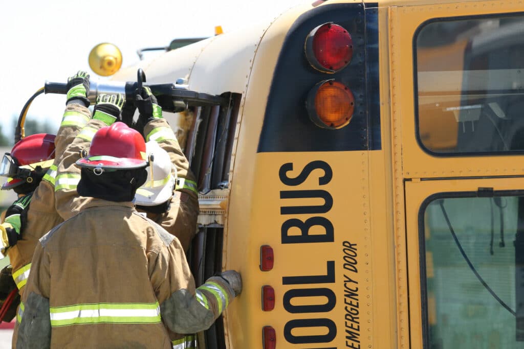 Firemen extricating students from a school bus on its side due to an accident.