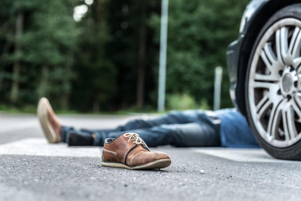 Scene of a pedestrian accident. A pedestrian is lying on the ground in front of a car with his shoe in focus.