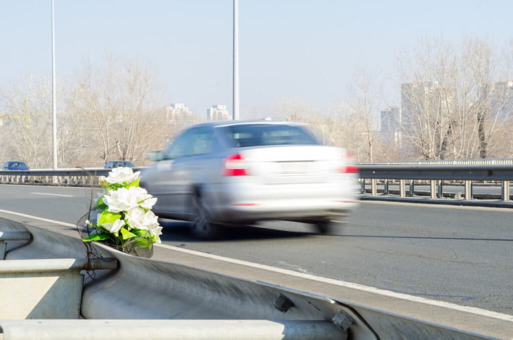 A speeding car at a site of a previous traffic accident indicated by some white roses.