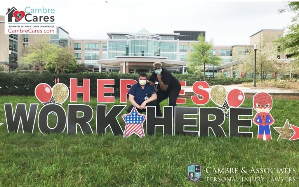 Two healthcare workers pose in front of a "Heroes Work Here" sign outside Tranner Medical Center, recognizing frontline workers. Glenn Cambre and Cambre & Associates show appreciation for healthcare professionals through community initiatives.