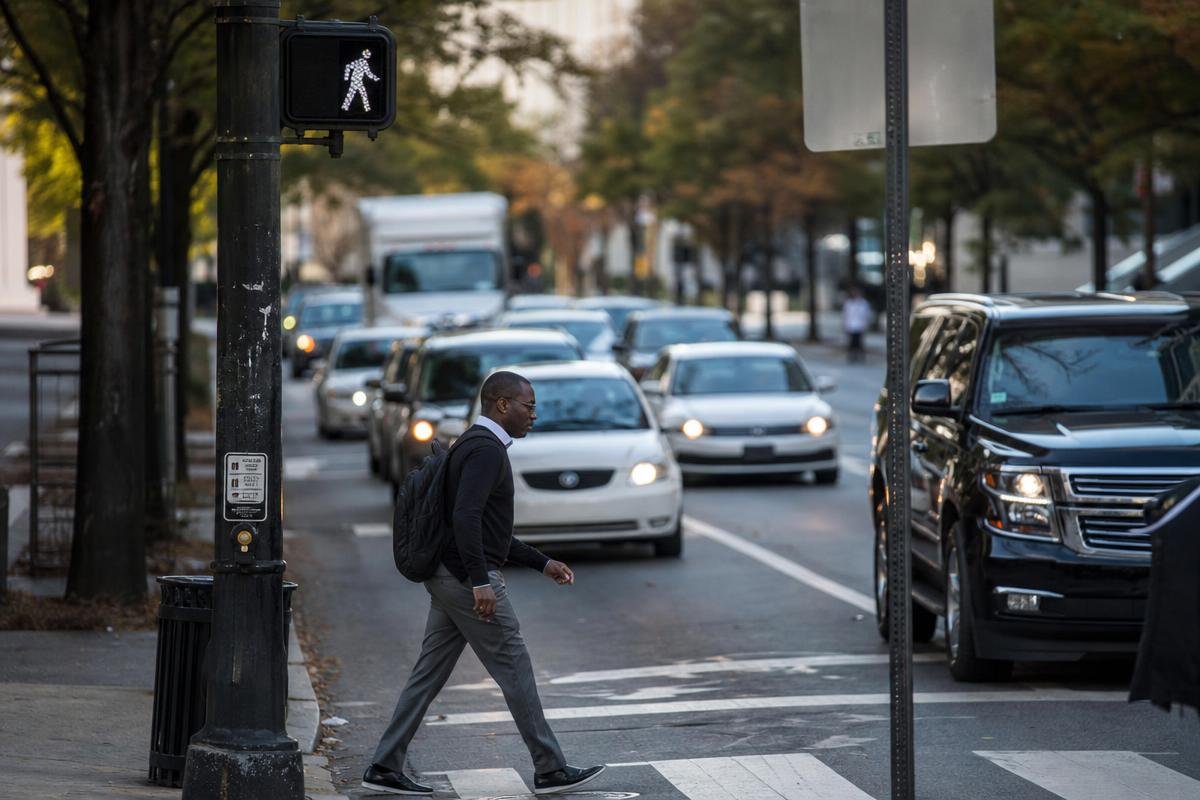 Pedestrian crossing a marked crosswalk beside congested city traffic